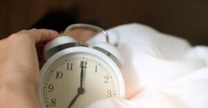 a bed and alarm clock showing that getting enough sleep can book your energy