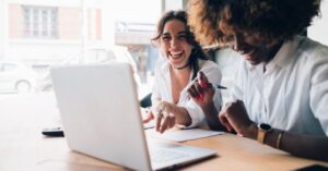 two women working at a desk laughing. 